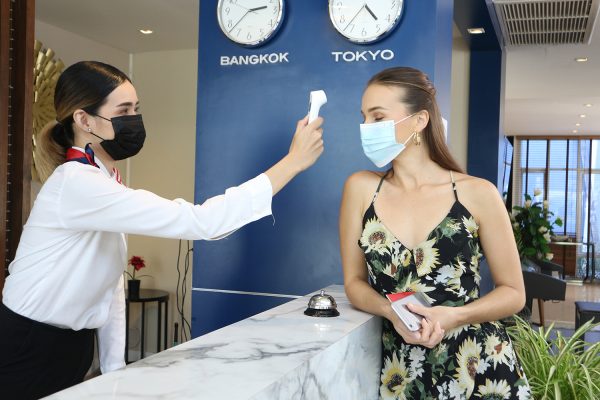 tourist woman and receptionist at counter in hotel wearing medical masks as precaution against virus. Young woman on a business trip doing check-in at the hotel A tourist woman and receptionist at counter in hotel wearing medical masks as precaution against virus. Young woman on a business trip doing check-in at the hotel
